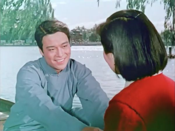 A viwe of the young man on the boat from behind the shoulder of the woman in orange sweater.