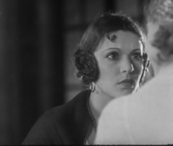 A woman dressed in black and with a serious expression on her face is deep in conversation with another woman, whose back is turned.