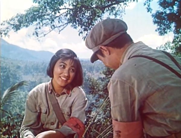 View of the two young soldiers from behind the shoulder of the male, showing the young woman’s face in full.