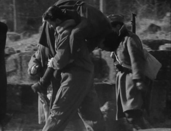 A soldier in uniform carries a fellow wounded officer across his shoulder out of battle as two army men walk by their side.