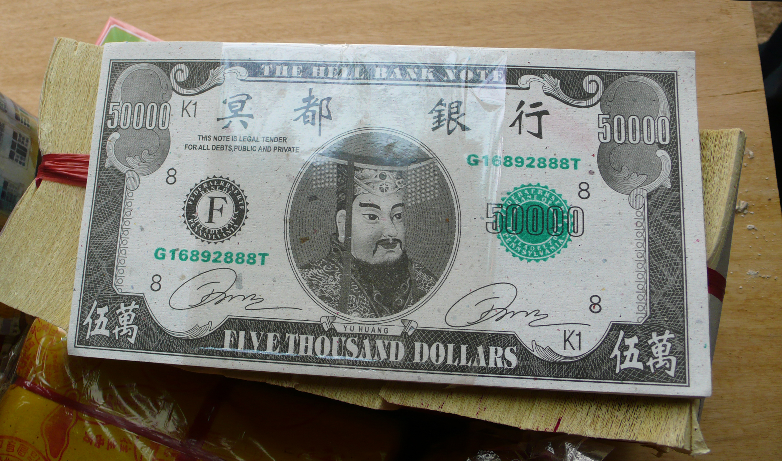 A stack of paper money resembles American dollars, but bear the inscription Hell Notes. A Chinese deity, the Jade Emperor, is printed at the center.