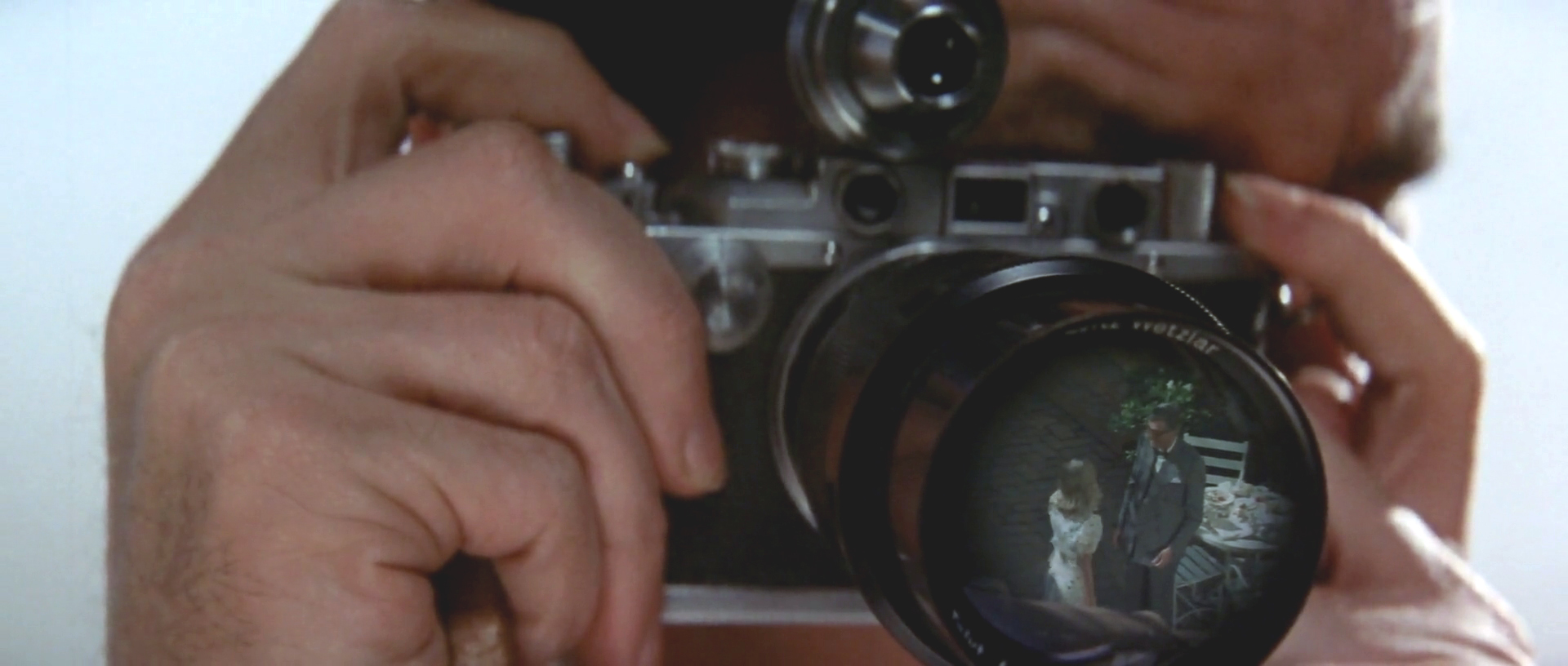 A close shot on Jake with a camera held up to his face with the reflections of his subjects visible in the lens.