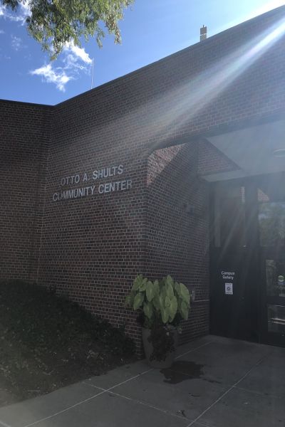 A sunbeam shines on a brick building. A sign on the wall says Otto A. Shults Community Center, and a door sign says Campus Safety.