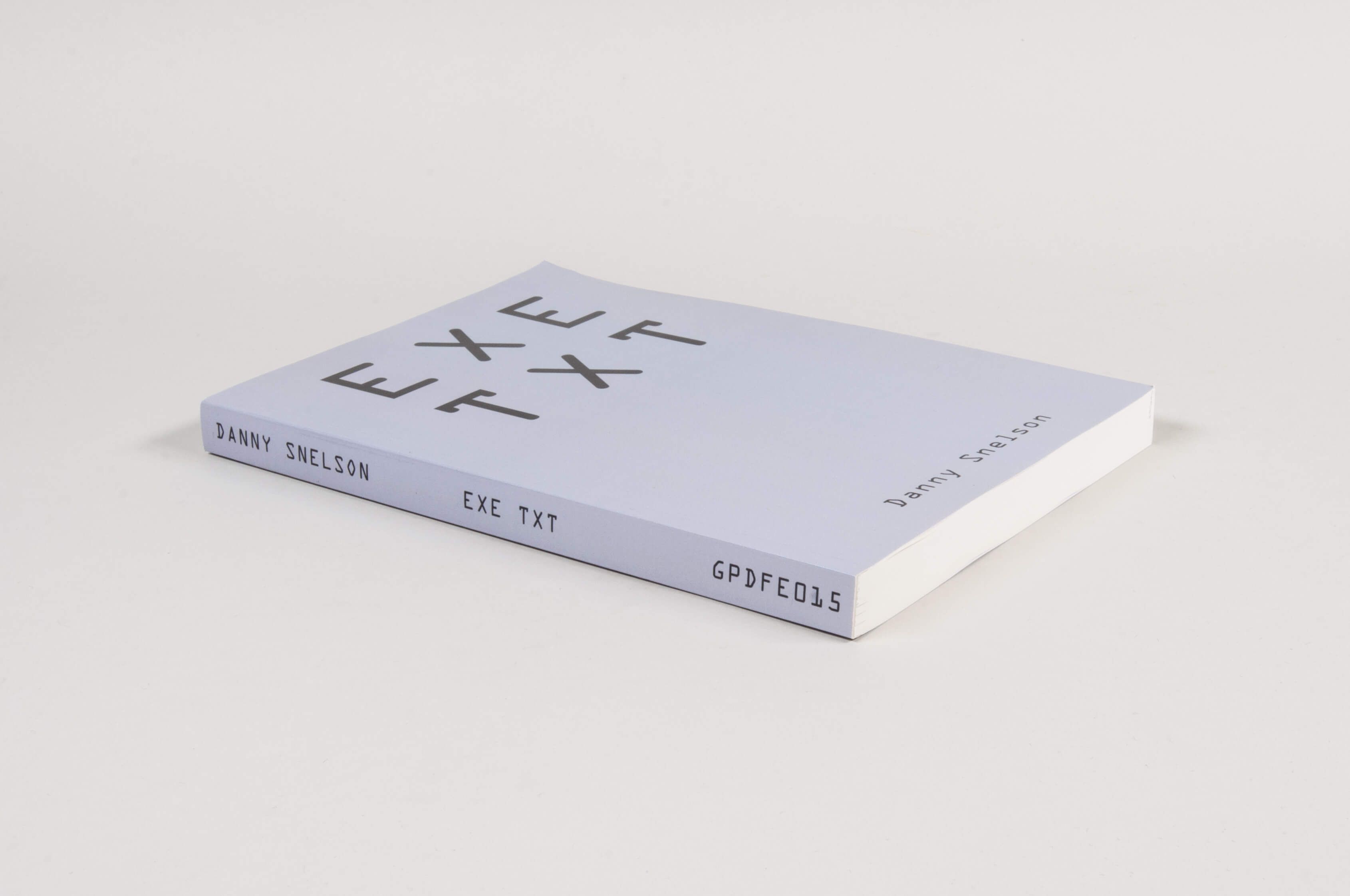 A light grey book titled “EXE TXT” by Danny Snelson, with the title and author’s name on the spine. The book is placed on a white surface.