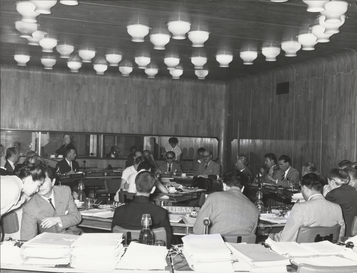 Photograph of delegates convening around circular table with a circle of ceiling lights above it.
