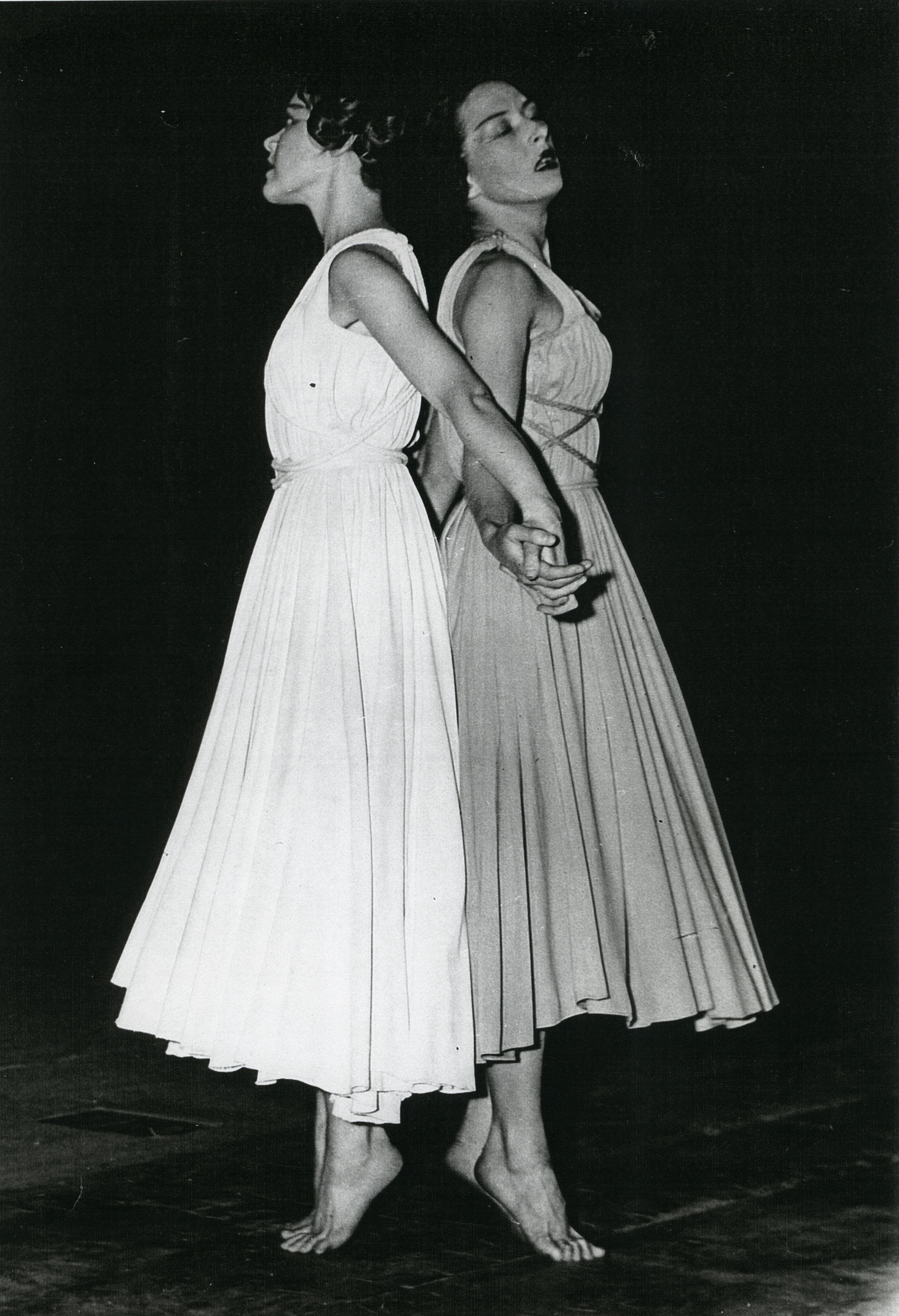 Two dancers in long dresses perform back-to-back.