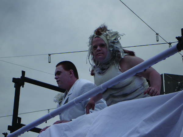 Two performers dressed in white on scaffolding looking out below them.