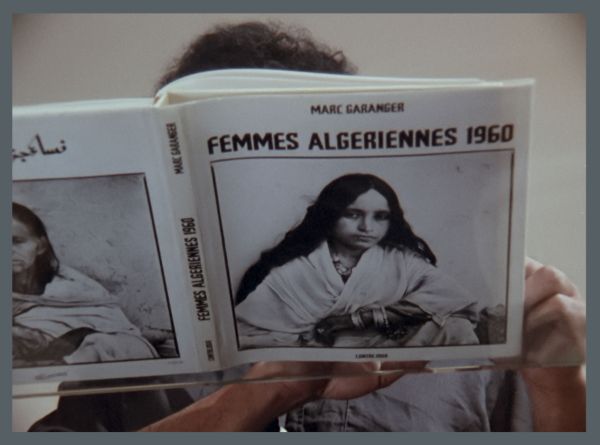 A person reading the book Femmes algeriennes 1960. The book’s cover features a woman’s portrait, and the reader’s head just barely peaks out.