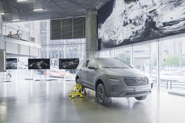 A clean indoors space with large windows. Inside the exhibition-type space is a car with several screens surrounding the car.