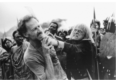 The exhibit features a scene from the movie “Cobra Verde” depicting Werner Herzog and Klaus Kinski in action, with one man holding a sword at the other’s neck. African native people are seen in the background holding spears and shields, capturing the dramatic setting of the film.