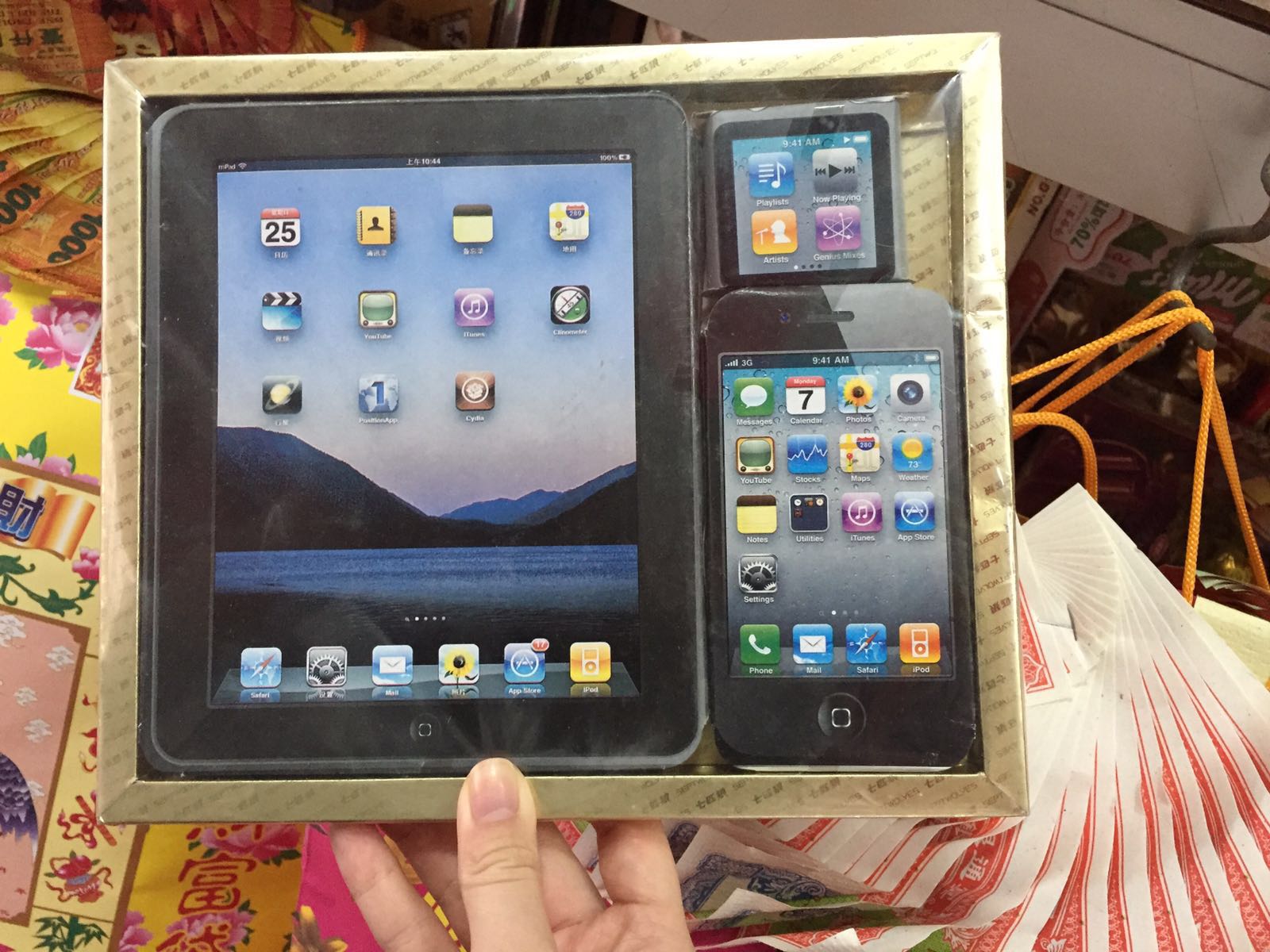 A hand holds a box set of paper items. These are copies of an Apple iPad, iPhone, and Apple Watch. The items appear to be real.