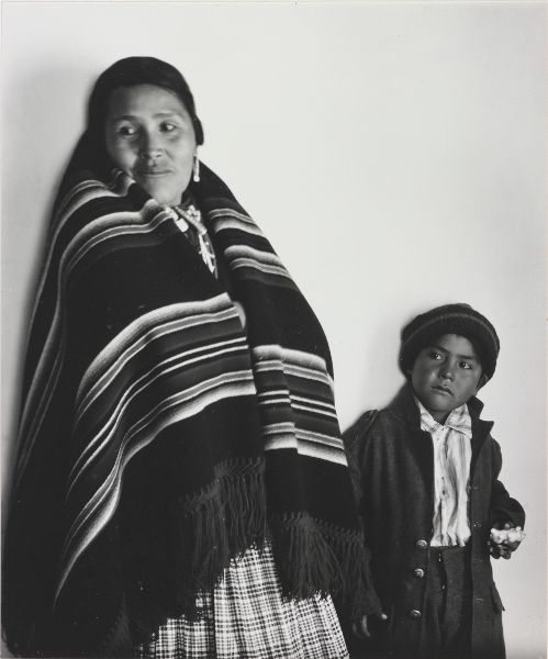 A woman draped in a striped blanket looks over her right shoulder, away from a child on her left gazing in the same direction.
