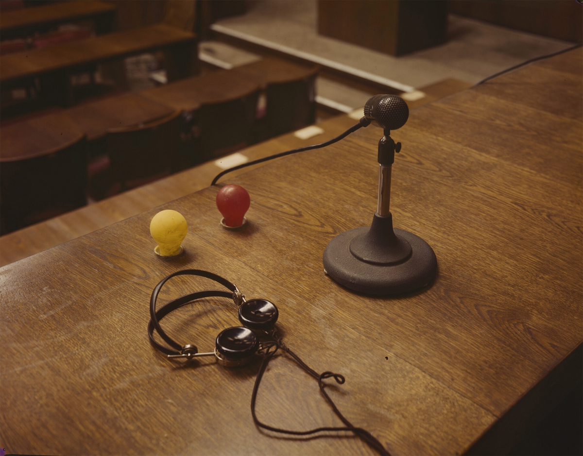 Photograph of headphones, microphone, and yellow and red light bulbs attached on the podium.