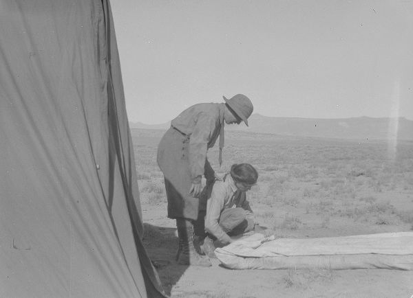 A woman in a white dress stands in a prairie landscape, facing into the frame from the left, the top of her head level with the flat horizon. 