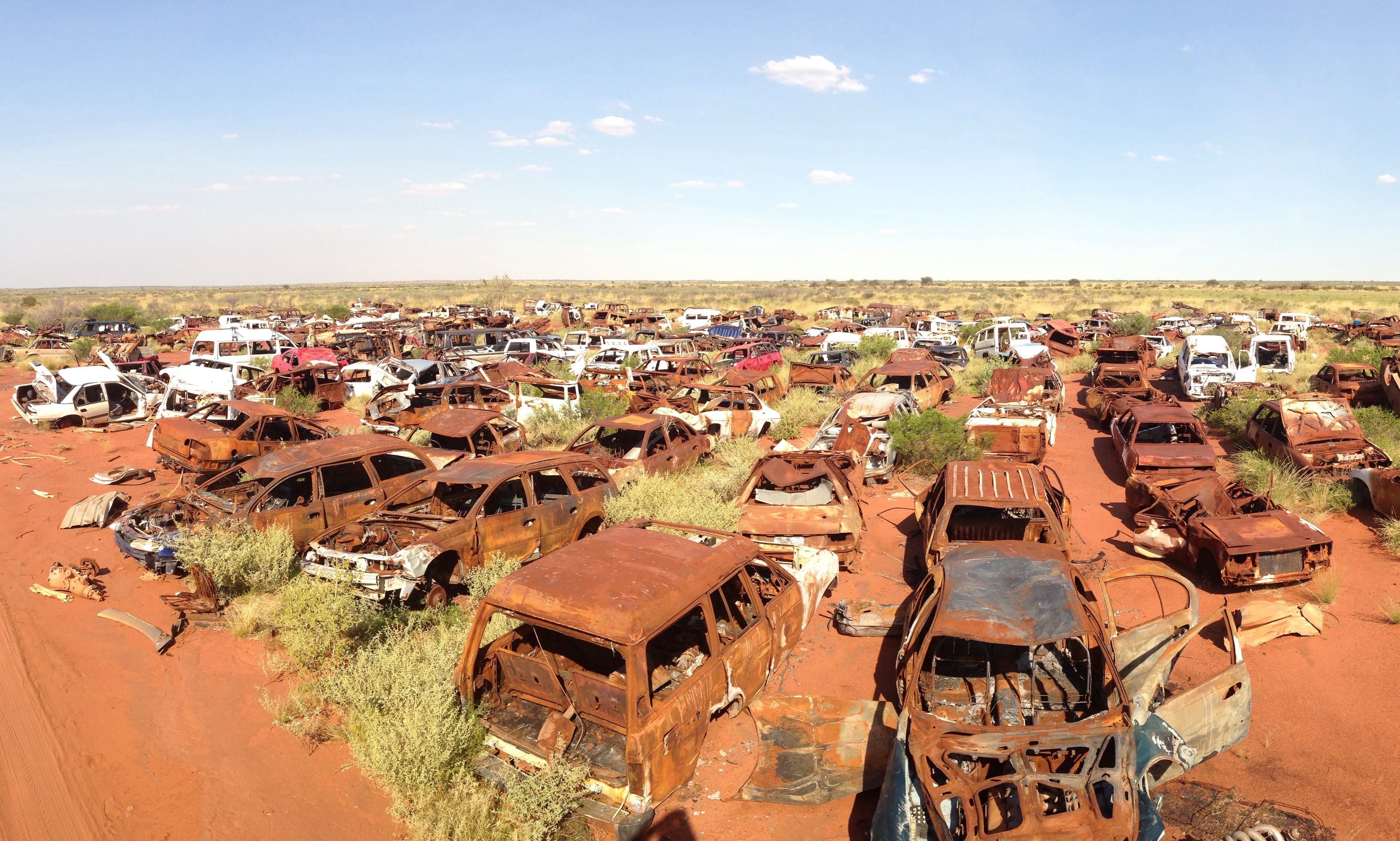 Panoramic view of hundreds of car bodies and parts lined up and organized on a sunny day. There are two roads leading through the area.