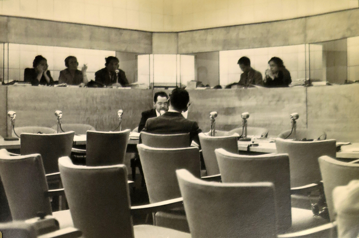 Photograph of male and female interpreters wearing headphones behind enclosed glass booths.