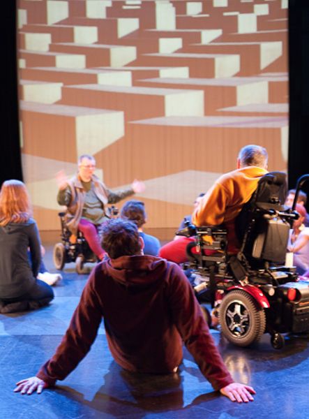 A small group of people, some in wheelchairs, in front of a video screen.