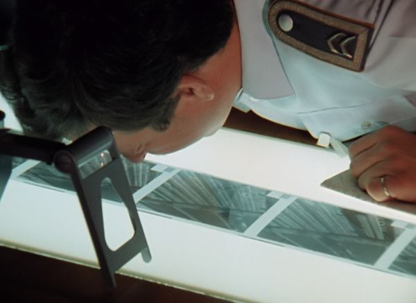 A person in a military uniform bends over a backlit table to peer closely at images.