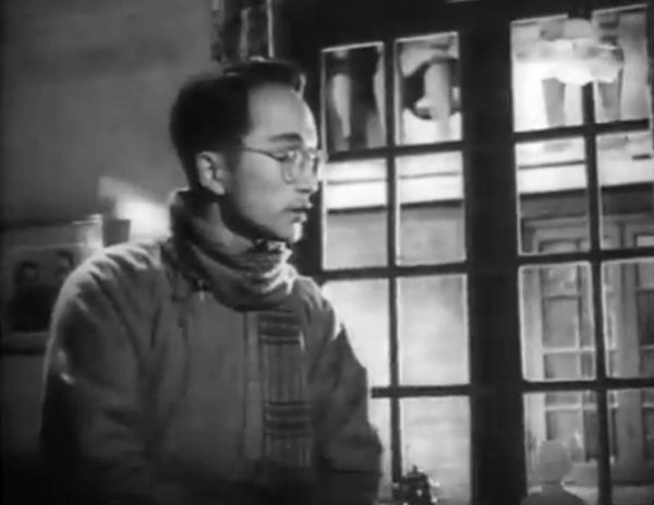 Bespectacled man in coat and scarf in middle distance.