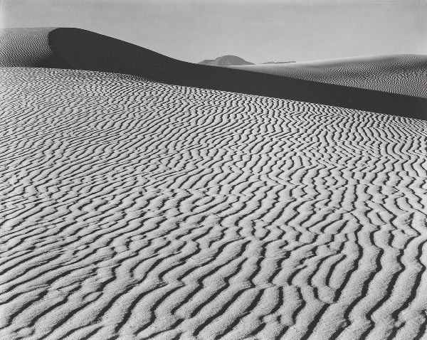 Rippling waves of sand appear as uneven vertical stripes in front of a shadowed dune, which creates thick, dark horizontal line at high horizon.