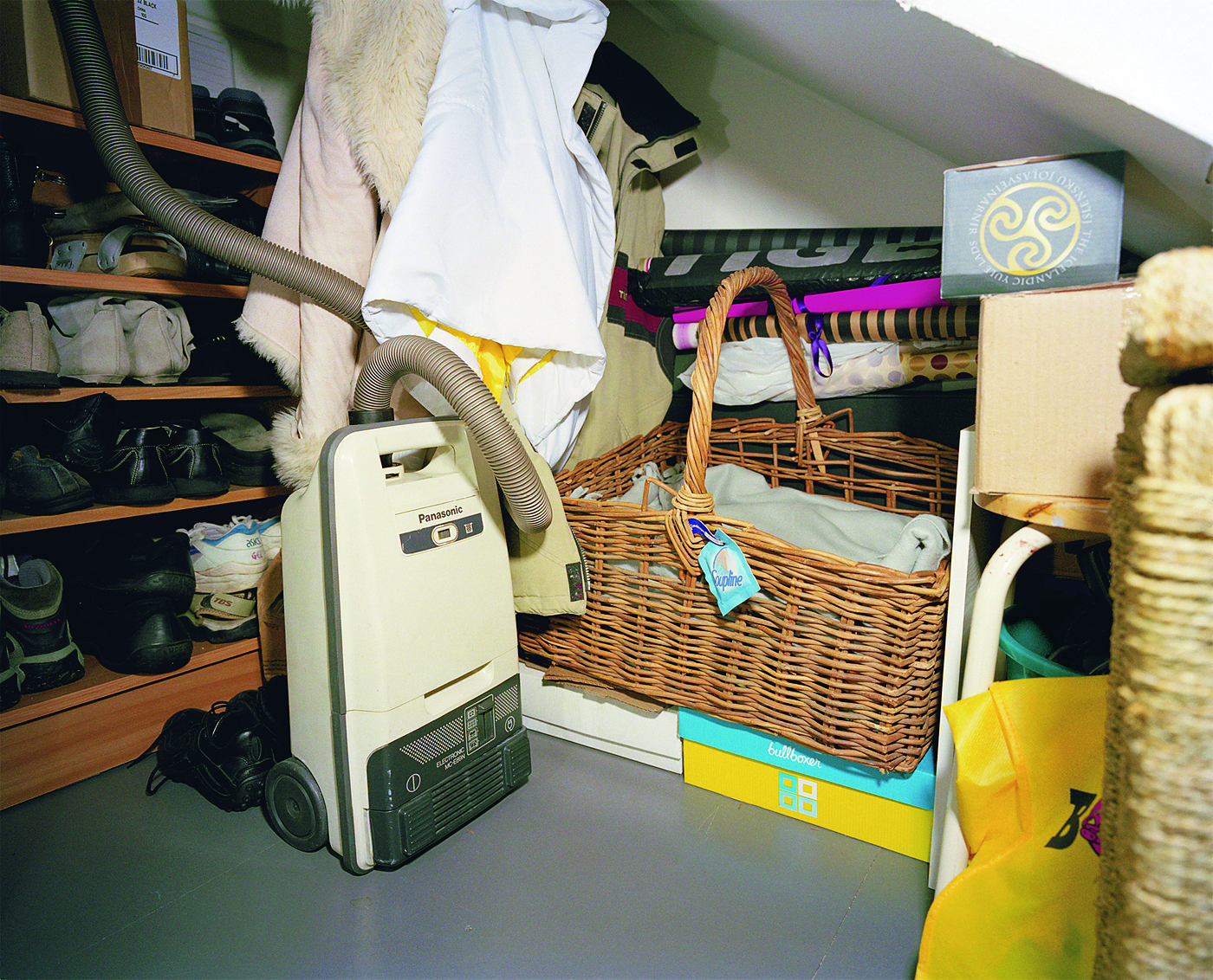 A cluttered storage area with a vacuum cleaner, wicker basket, shoes, and various household items.