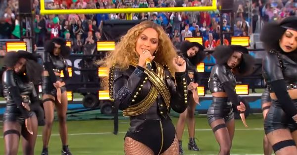 Beyoncé standing on the field singing in the middle of her dancers as they make their way to the stage.