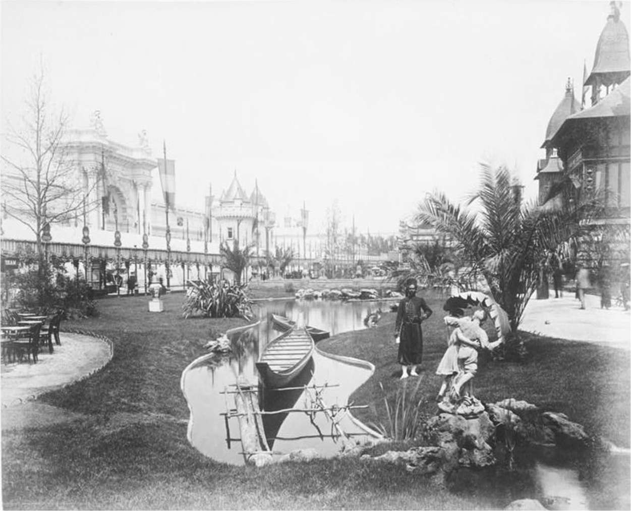 A photograph of the garden of Palais des Colonies with a statue of a couple and a pond with boats.