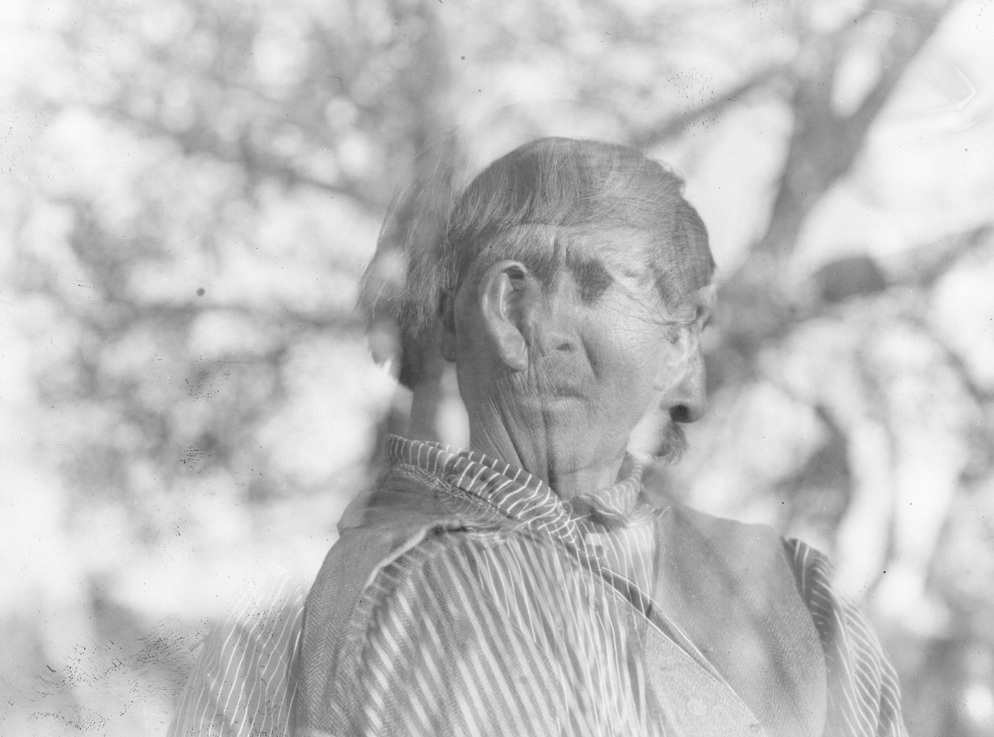 Double-exposed image of facing and profile headshots of an older Native American man.