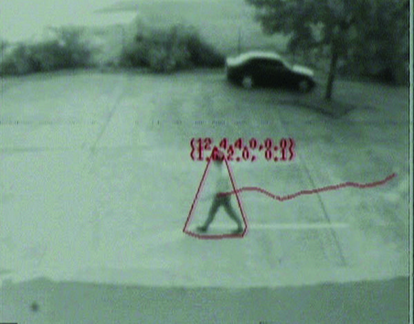 A computer vision view of a parking lot or similar. A human walking across the space is being tracked. A car in the background next to a tree.