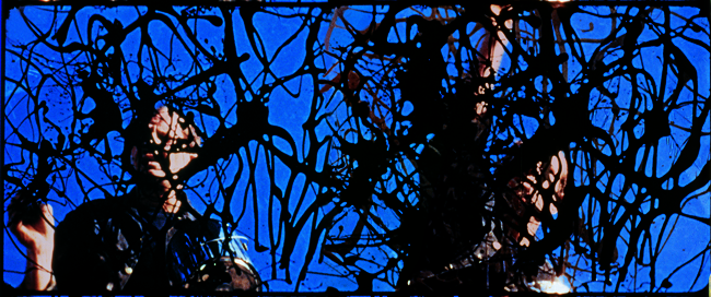 The exhibit features a 1951 film still capturing Jackson Pollock and another individual engaged in what seems to be painting on glass, using black strokes of paint.