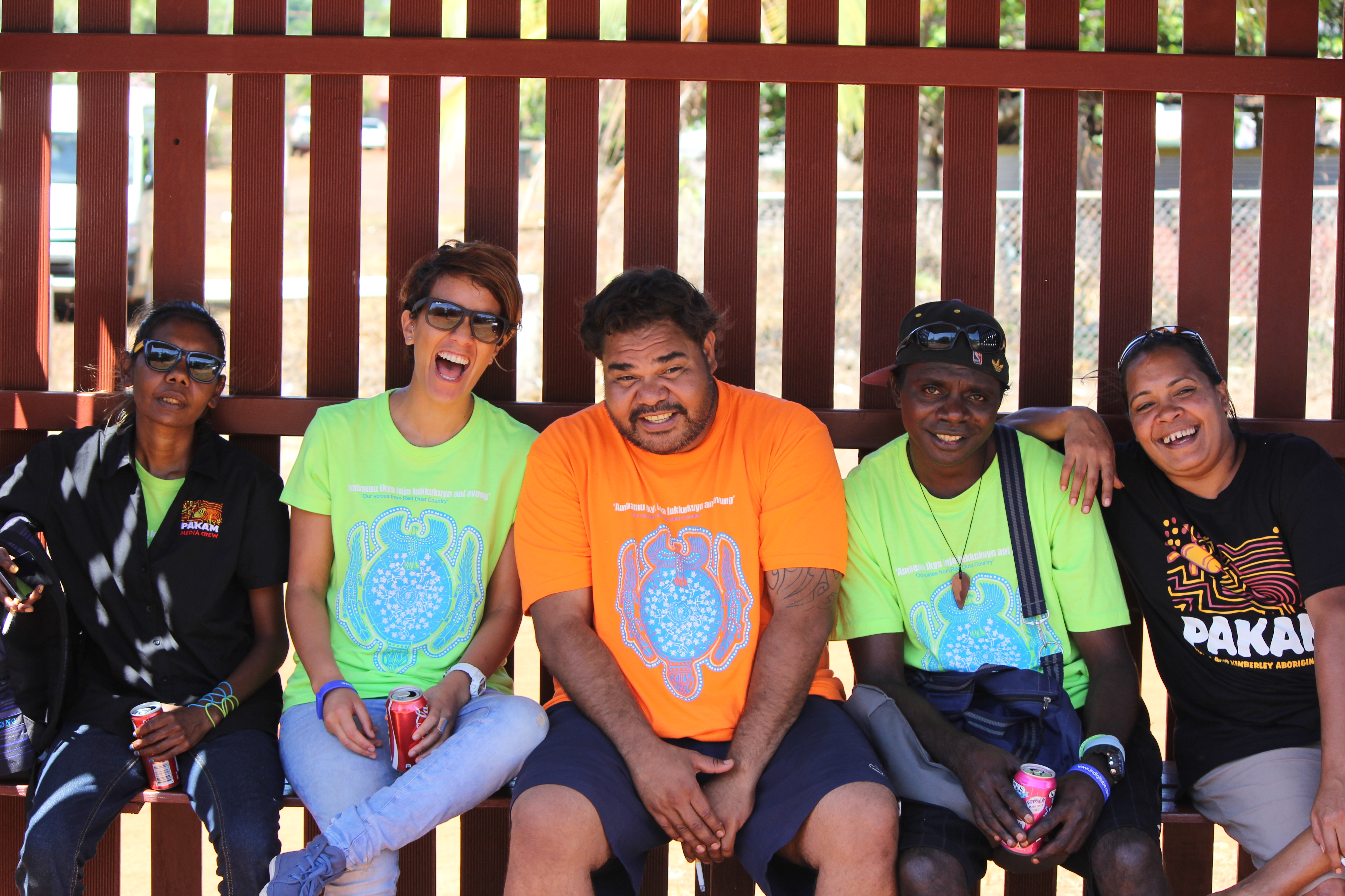 Five members of the PAKAM crew are sitting on a bench, smiling and laughing into the camera together.