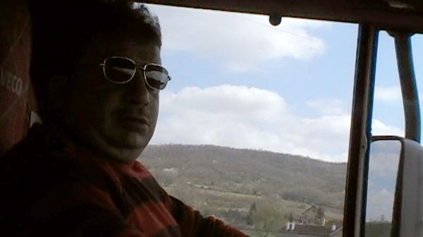 A shot of a man driving a truck from the perspective of a passenger beside him.