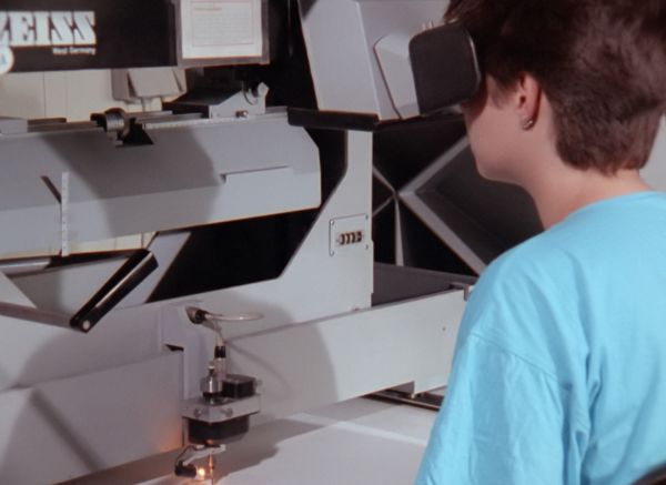 A person looks into a large white machine through mounted binoculars.