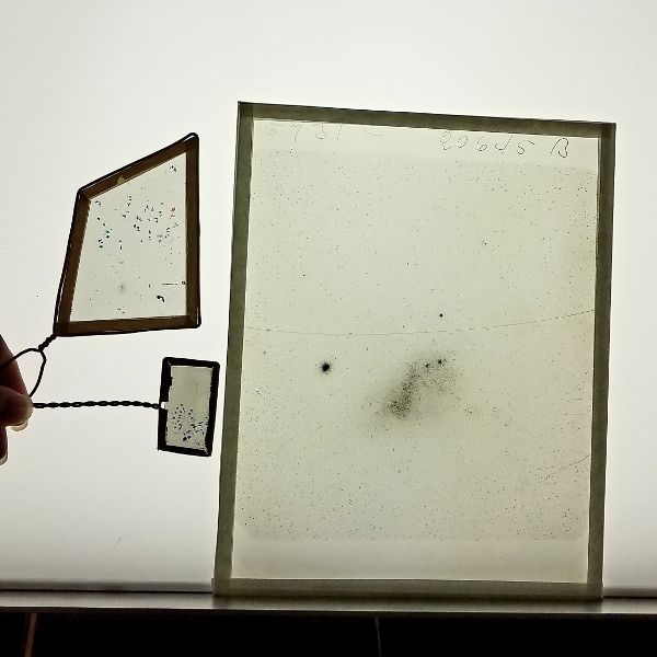 A photographic plate with a cluster of dots depicting the night sky. To the left is a rectangular transparent viewing device with similar dots.