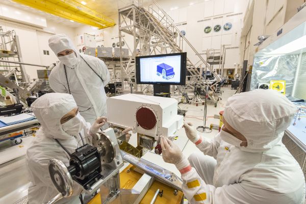 Three masked scientists around a technical device, installing an imaging instrument in a laboratory setting.