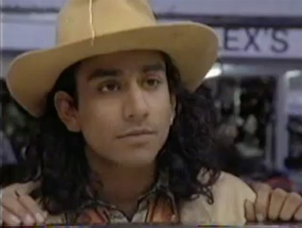 Close-up shot of actor Naveen Andrews with shoulder-length black, wavy hair, wearing a cowboy hat.