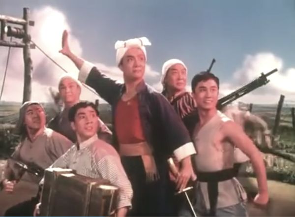 Six young men pose together in a group looking triumphant, some holding weapons, others holding luggage.