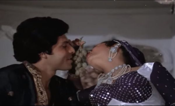 Man and woman leaning toward another and kissing the grapes he holds between their faces.