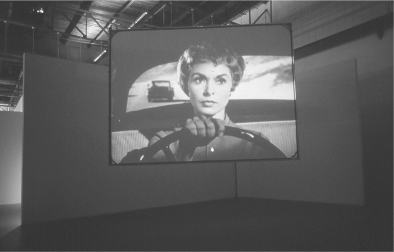 A photograph of a projector playing a scene of a woman driving a car.