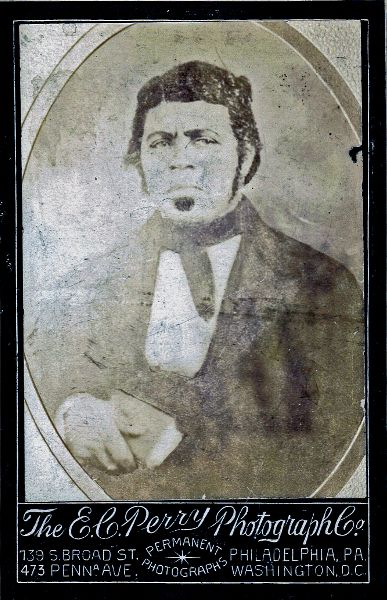 Black and white photograph of a man in nineteenth century suit holding a book to his body