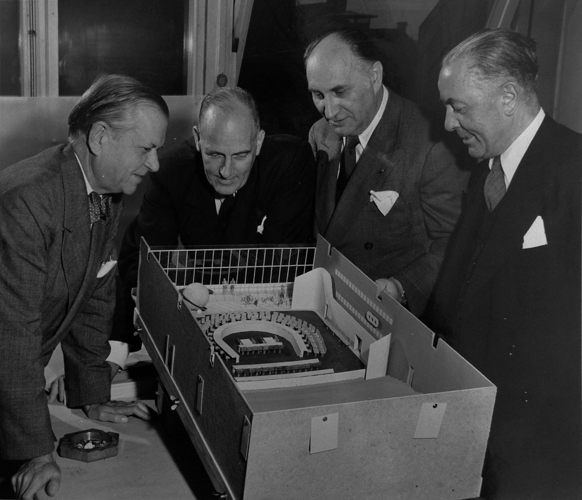 Photograph of four men looking into an open architectural model of the ECOSOC Council Chamber.