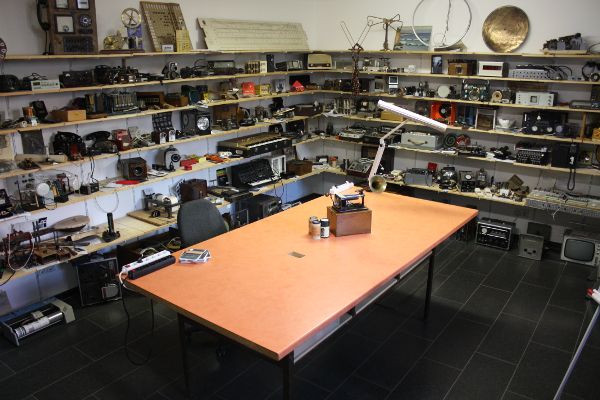Nearly empty work table in the center of a room lined entirely with shelves that are packed with a variety of small technical equipment.