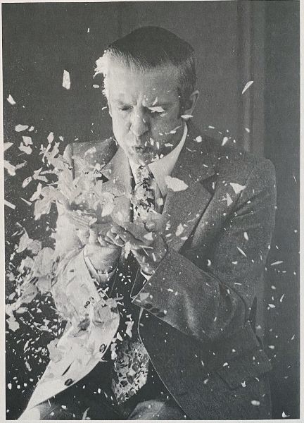 Man in suit and tie blowing paper scraps from his hands