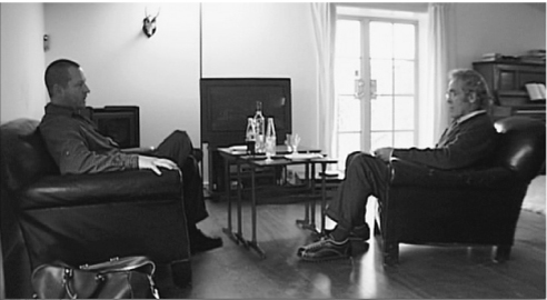 The exhibit captures an image of two men in formal attire seated in chairs within a room, deeply engrossed in a serious conversation.