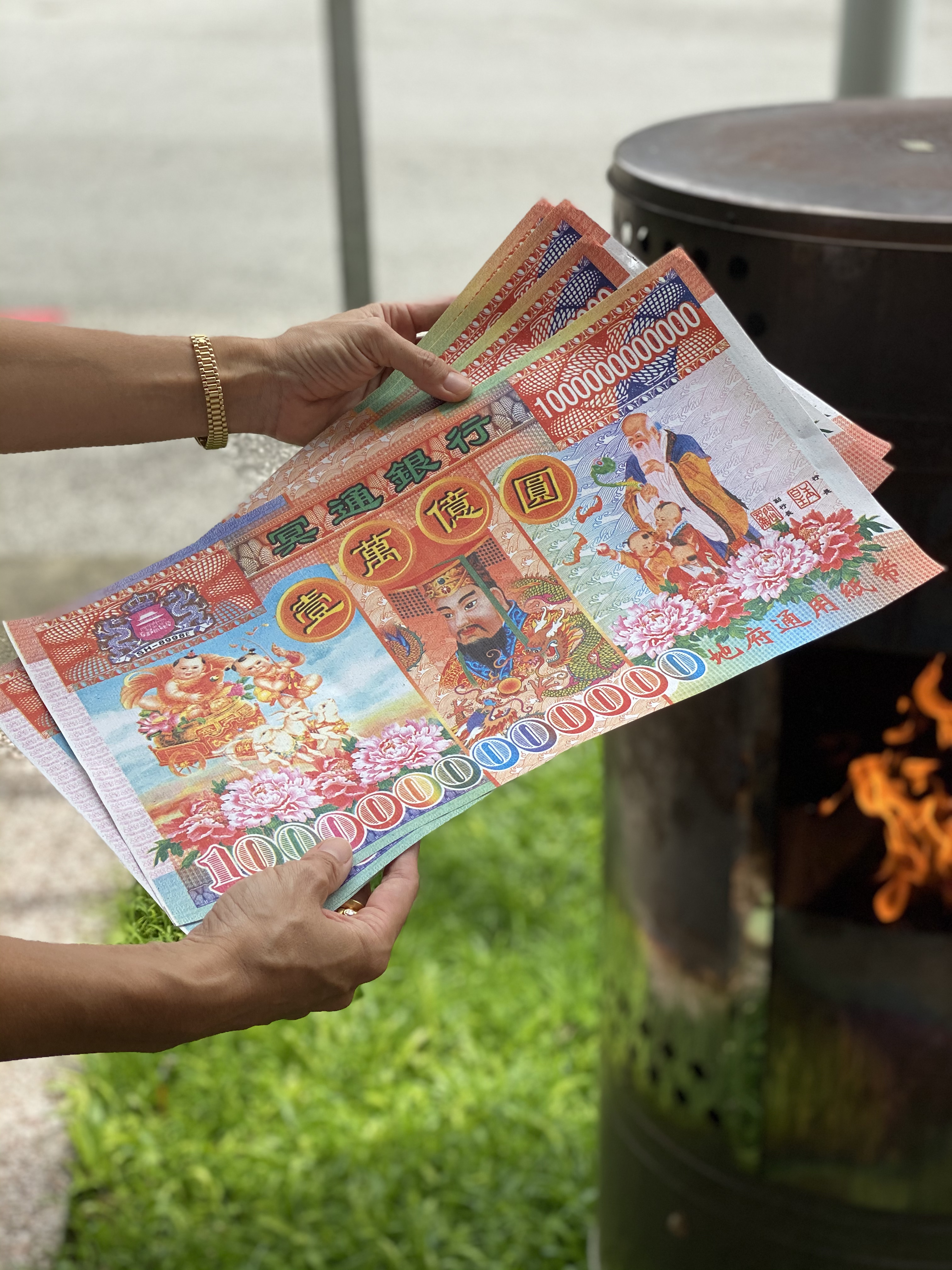 Two hands hold large, colorful and ornamented paper bills. The denomination is one trillion dollars.