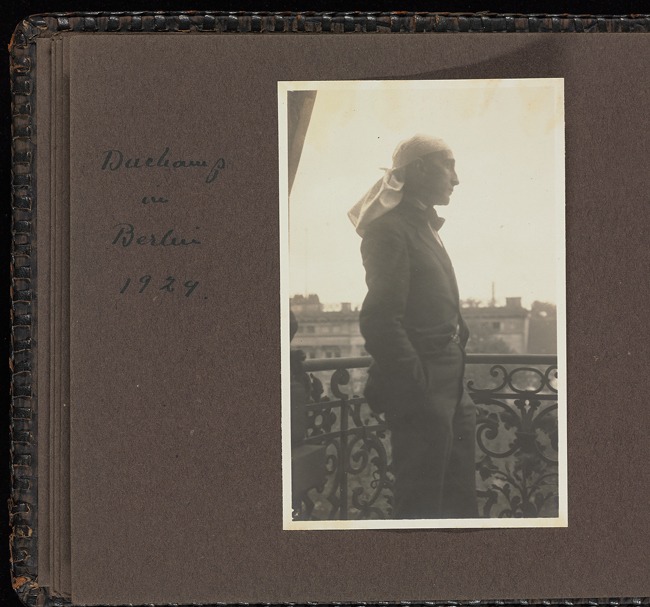 The exhibit features a photograph of Marcel Duchamp, dressed in a suit and tie with a cloth tied around his head, looking into the distance from the balcony of a room.