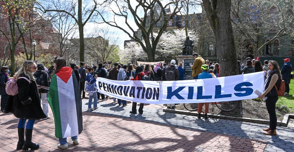 Student protestors at the University of Pennsylvania hold up a banner that reads “Pennovation kills.” A protestor in the foreground dons a Palestinian flag.