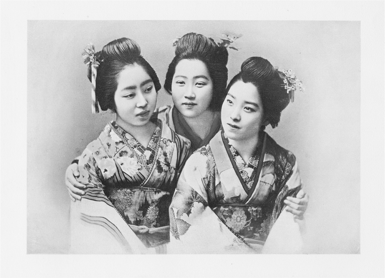 A comic diagram of three women in traditional attire, hair tied up with flowers and bands standing together besides each other with the woman in the middle holding the others by their shoulders.
