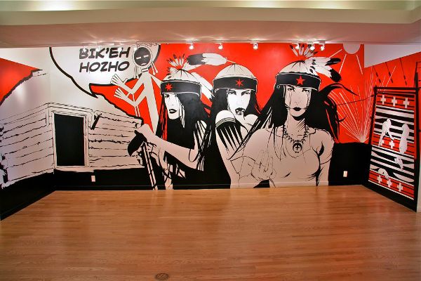 Mural on three walls depicting a hogan, three women, and a loom in graphic style.