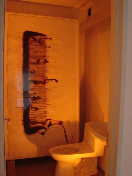 Sideview of a bathroom, specifically a toilet without a seat. On the wall beside it is a drawing of a hair comb, vertically oriented with teeth directed toward the toilet.